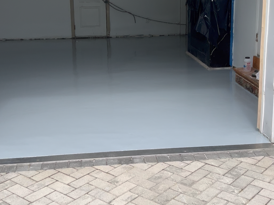 A freshly painted light epoxy gray garage floor with a brick paver driveway outside.