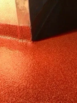 Close-up of a textured red epoxy flake floor with a corner where a gray wall meets a black door.
