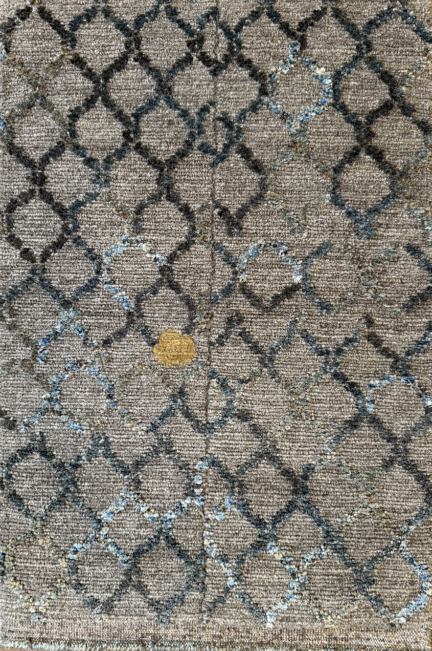 Close-up of a woven patterned rug with black geometric lines and a small yellow circular detail.