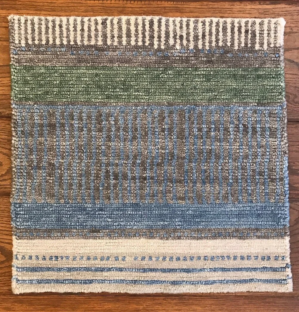 A rectangular woven rug with horizontal stripes in various colors including cream, green, blue, and brown, resting on a wooden floor.