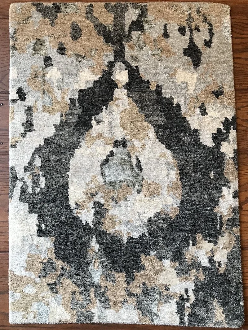 Abstract patterned area rug with black, beige, gray, and cream colors on a wooden floor.