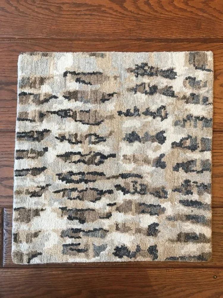 A rectangular patterned area rug on a wooden floor with beige, gray, and black abstract design.