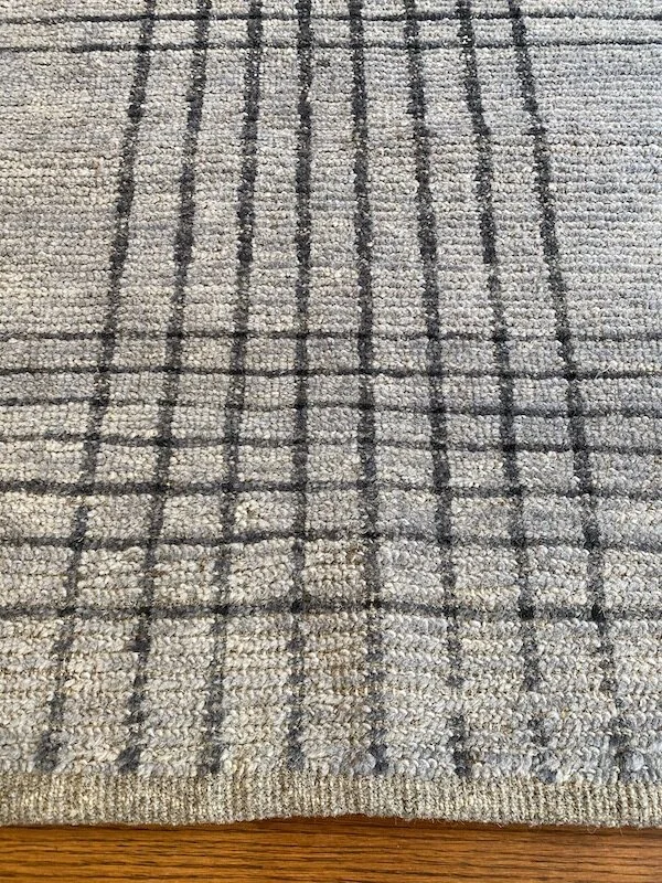 Close-up of a beige and gray striped textured rug on a wooden floor.