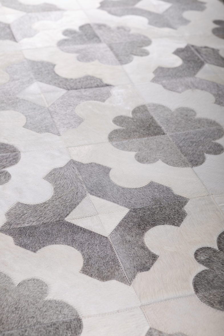 Close-up of a patterned tile or rug with gray and white shapes resembling clovers and geometric designs.