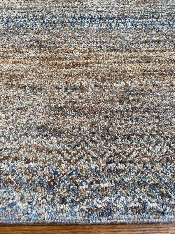Close-up of a multicolored textured area rug with shades of brown, beige, blue, and gray, on a wooden floor.
