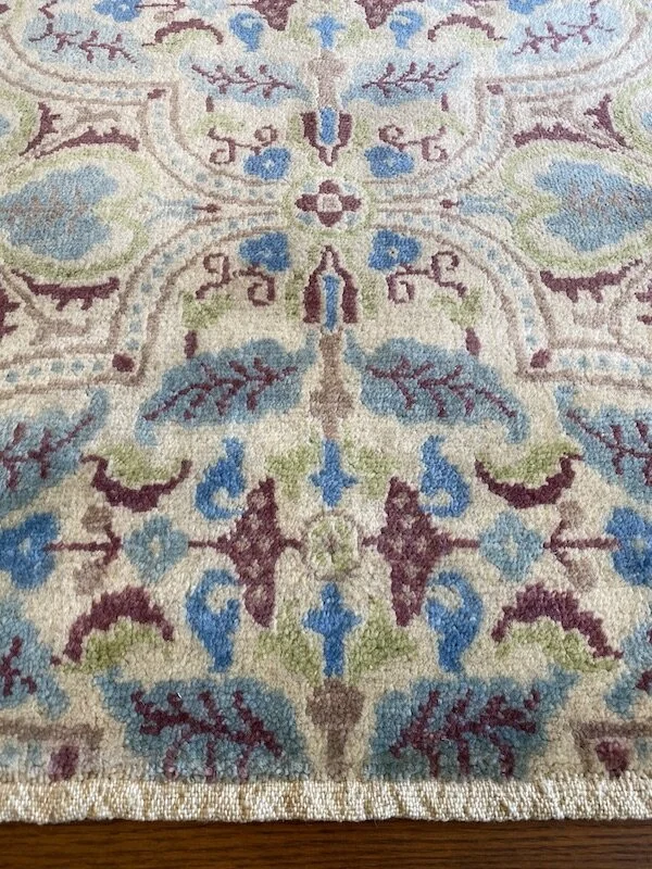 Close-up of a decorative rug with floral and vine patterns in shades of blue, green, purple, and beige.