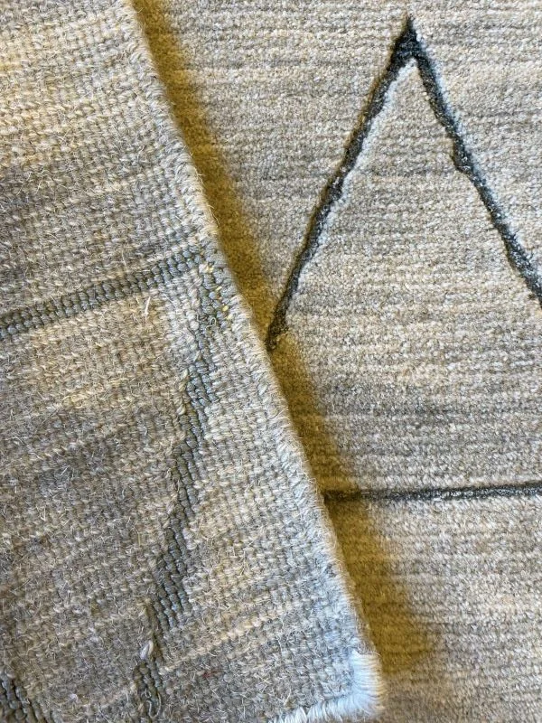 Close-up image of a sage rug and its back with geometric pattern