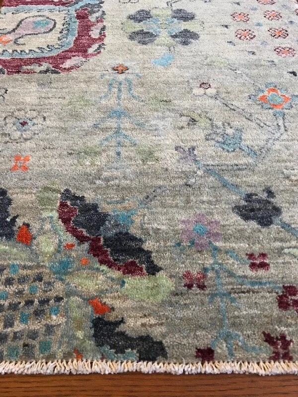 Part of a decorative area rug with floral and abstract patterns in various colors including black, blue, red, green, and purple, on a wooden floor.