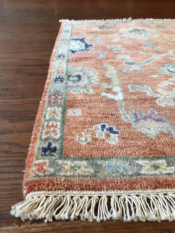Close-up of a decorative area rug with floral and geometric patterns on a wooden floor, featuring fringes on the edge.