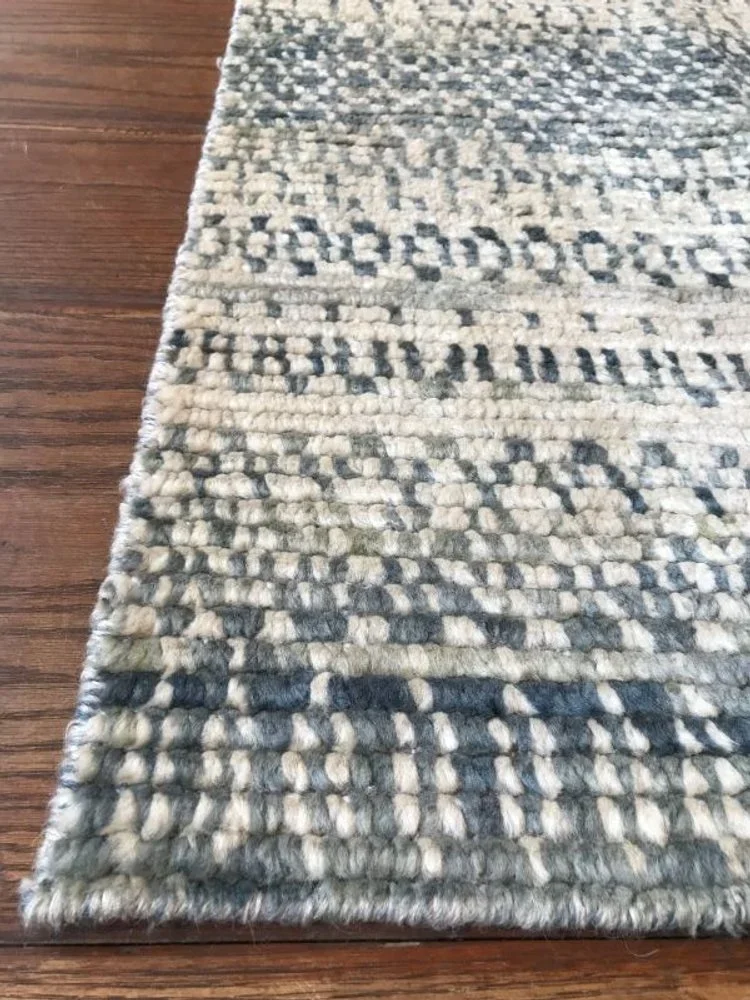 Close-up of a textured area rug with a gray, black, and white pattern on a wooden floor.