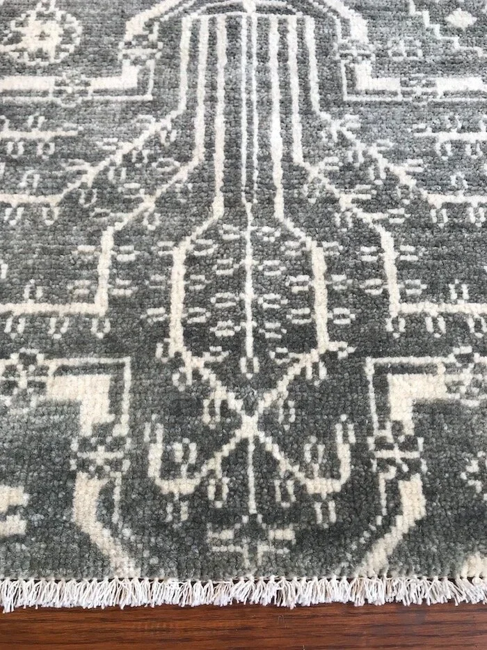 Close-up of a black and white patterned area rug with fringed edge, placed on a wooden floor.