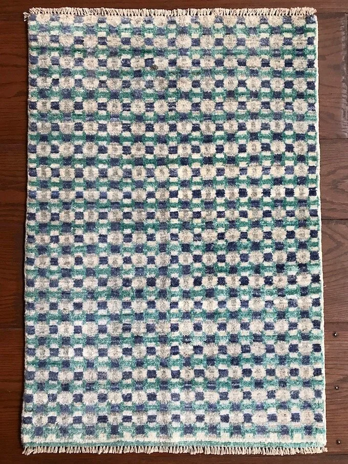 Patterned area rug with a checkered design in shades of blue, green, and beige, laid on a wooden floor.