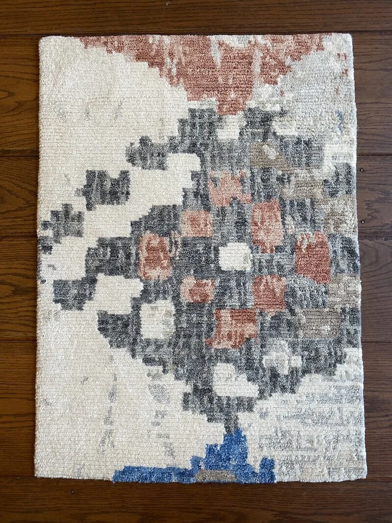 Abstract patterned area rug with shades of cream, black, pink, and blue on a wooden floor.