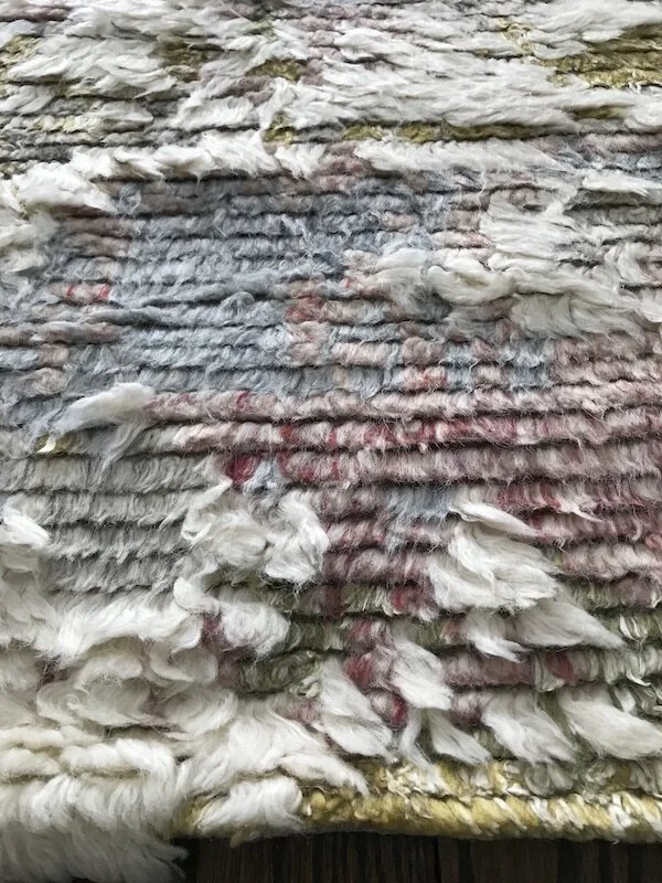Close-up of a woven textile made from various strips of fabric, featuring a mix of white, gray, and red colors with frayed edges.