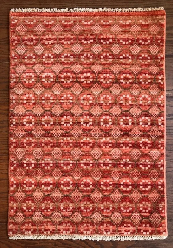 Red and pink patterned area rug with a repeating geometric design on a hardwood floor.