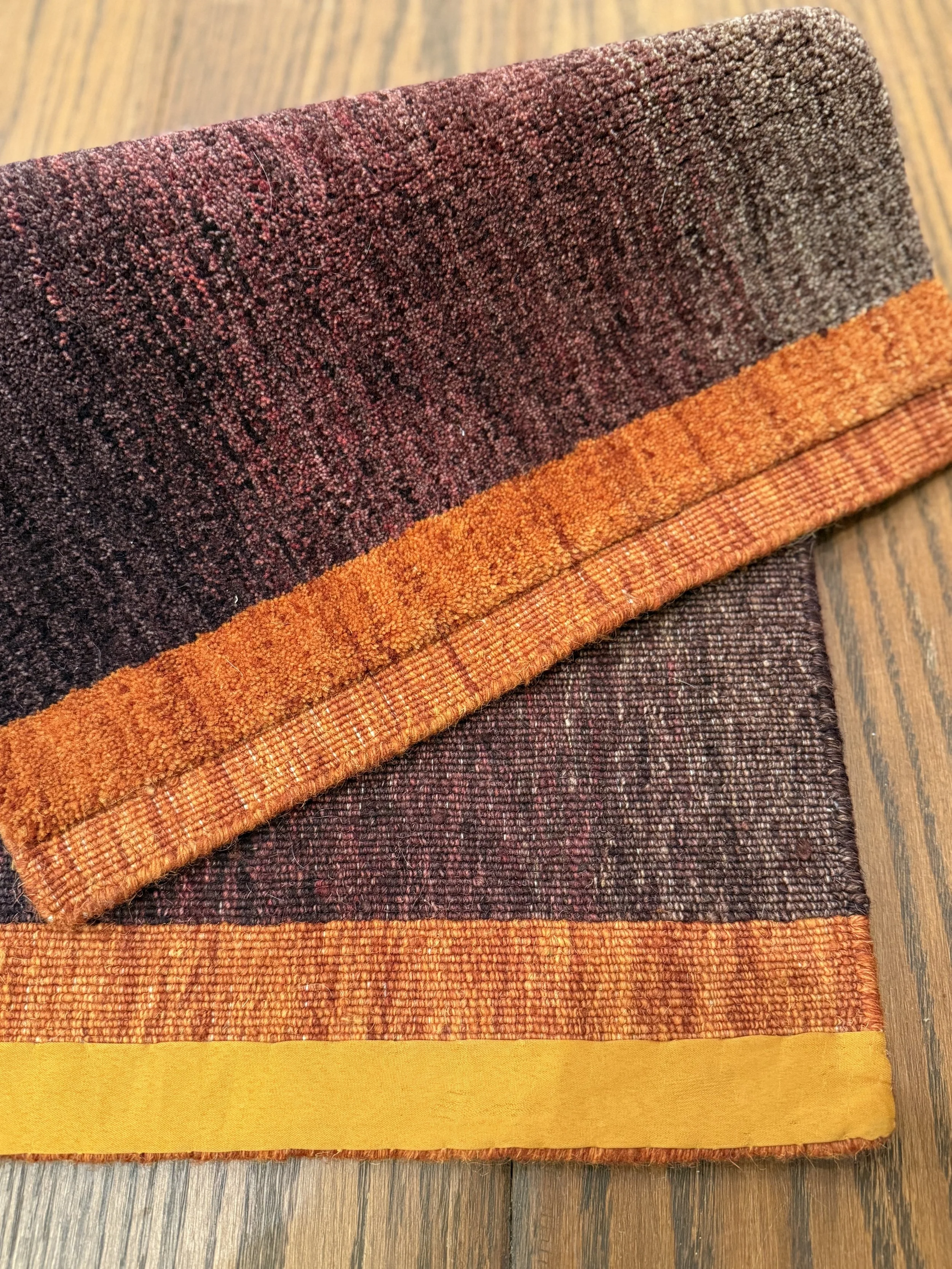A folded multicolored textured fabric with shades of brown, orange, and yellow, placed on a wooden surface.