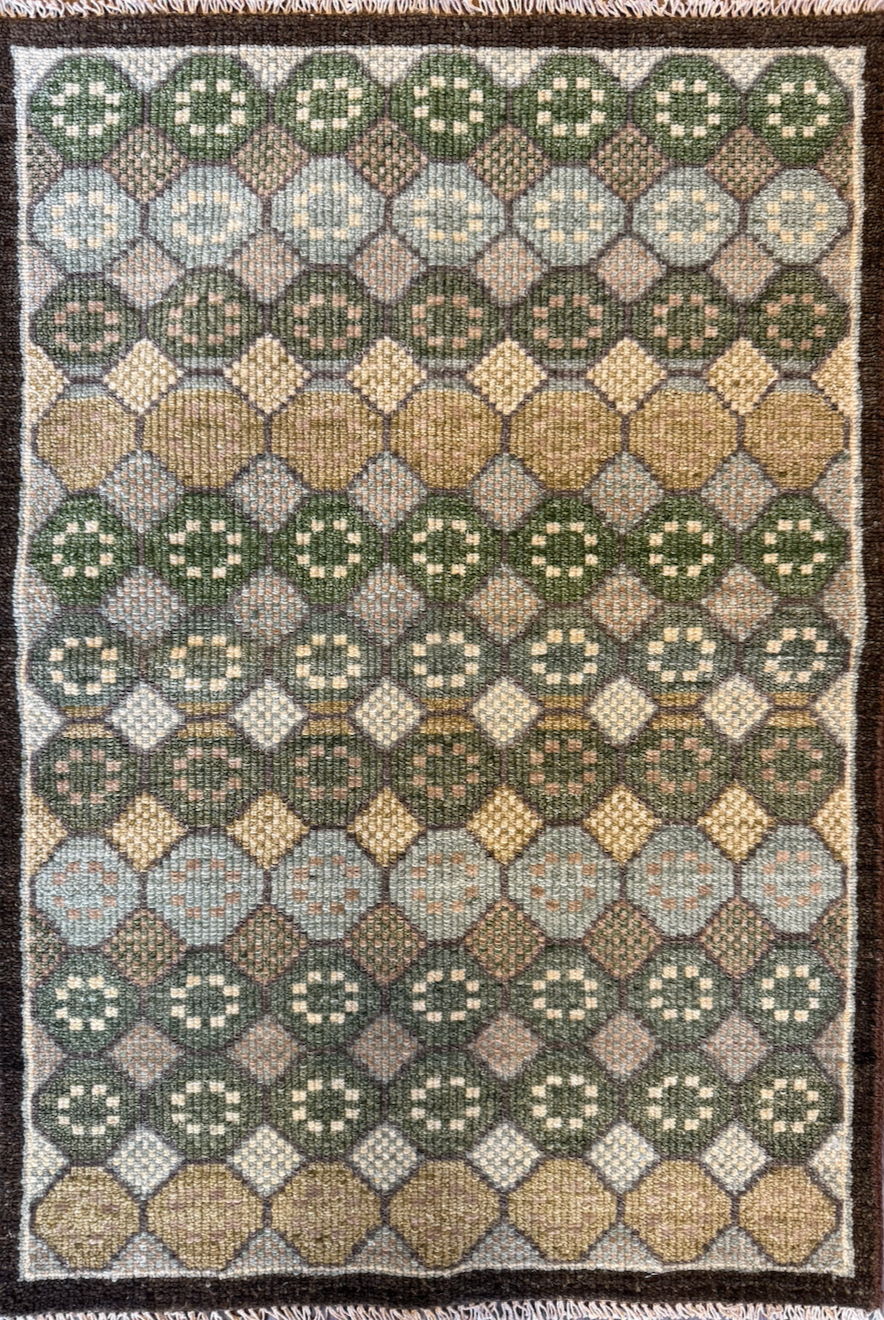 A rectangular woven rug with a geometric pattern of circles, diamonds, and squares in shades of green, yellow, beige, gray, and brown.