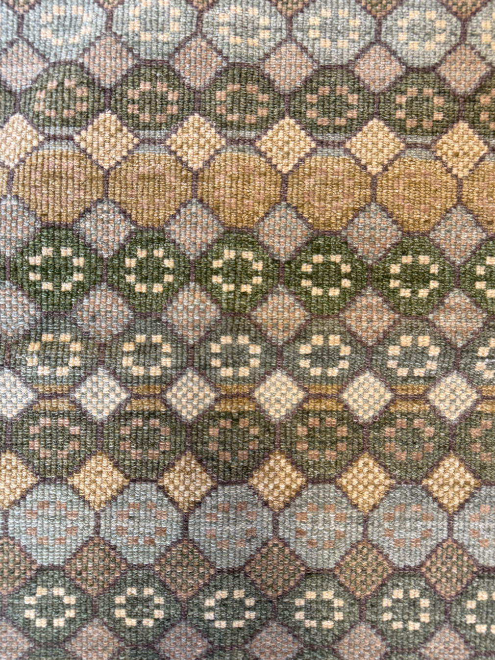 Close-up view of a woven fabric with a geometric pattern of circles and diamonds in shades of green, beige, pink, and brown.