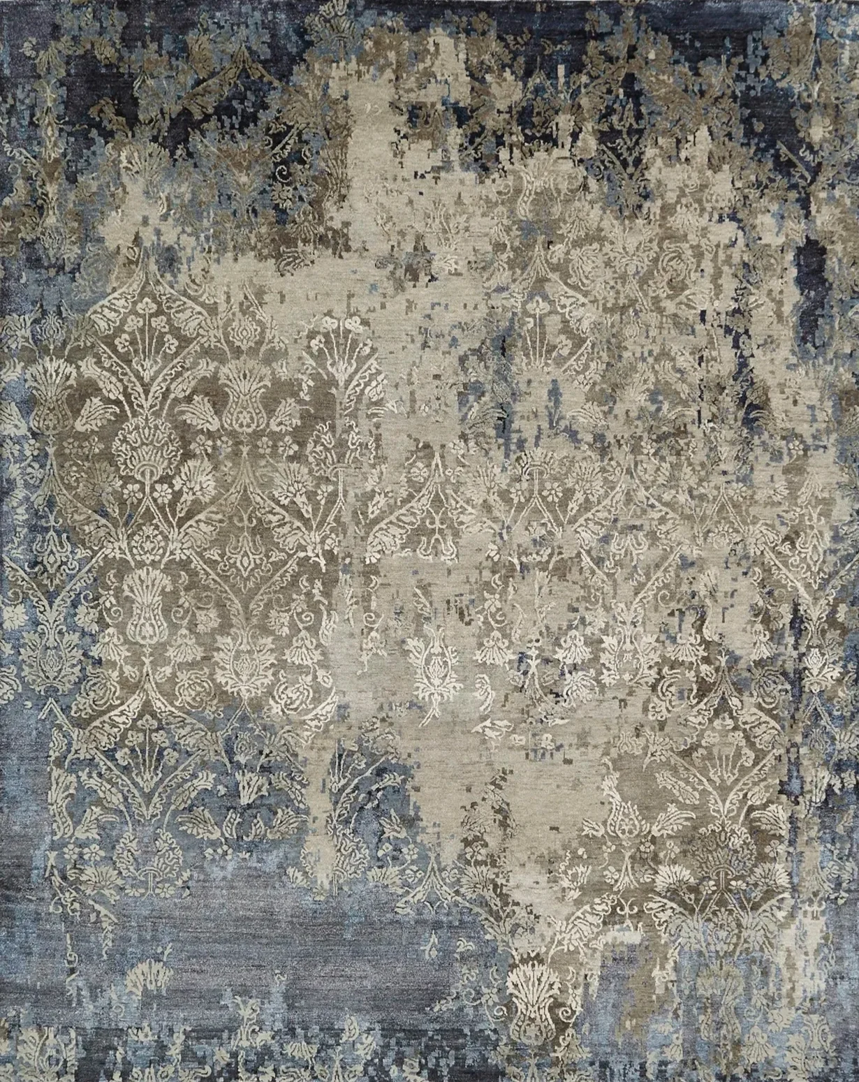 A large area rug with a distressed, vintage style featuring intricate floral and geometric patterns in beige, tan, and dark blue colors.