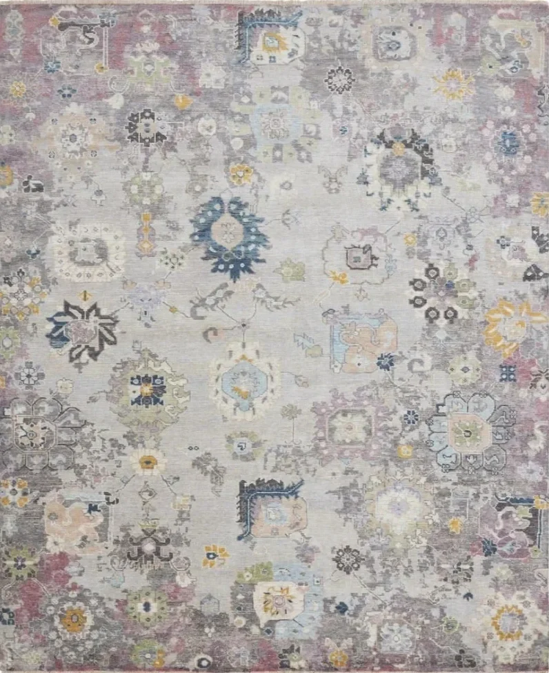 A vintage-style area rug with a faded, intricate floral and geometric pattern in pastel shades of pink, blue, yellow, and gray.