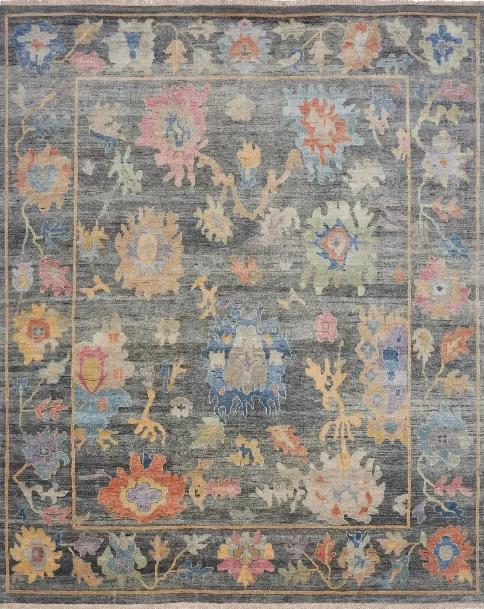 A colorful floral-patterned area rug with a gray background and floral motifs in pink, blue, yellow, orange, and purple hues, framed by a decorative border featuring similar floral designs.