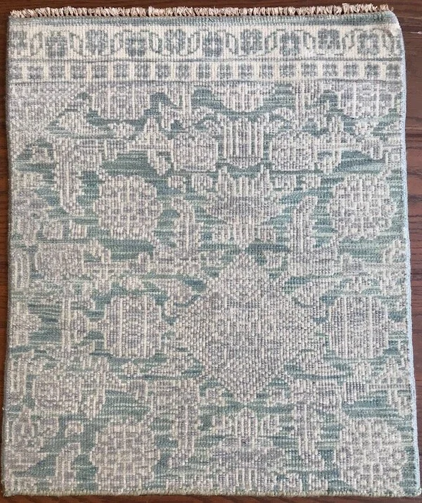 A patterned area rug with geometric and floral designs in shades of green, beige, and cream, placed on a hardwood floor.