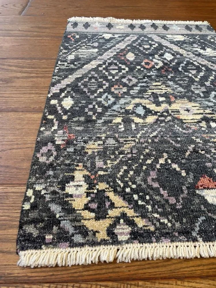 Close-up of a small patterned area rug with fringed edges on a hardwood floor.