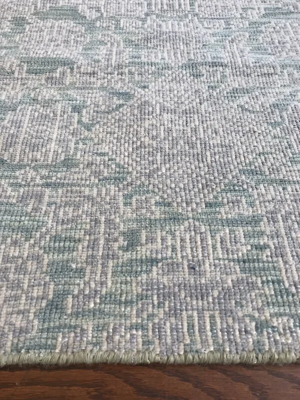 Close-up of a textured area rug with a geometric pattern in shades of blue, gray, and white on a wooden floor.
