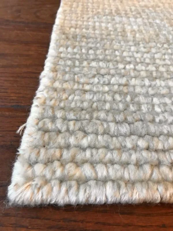 Close-up of a textured, light-colored woven rug on a wooden floor.