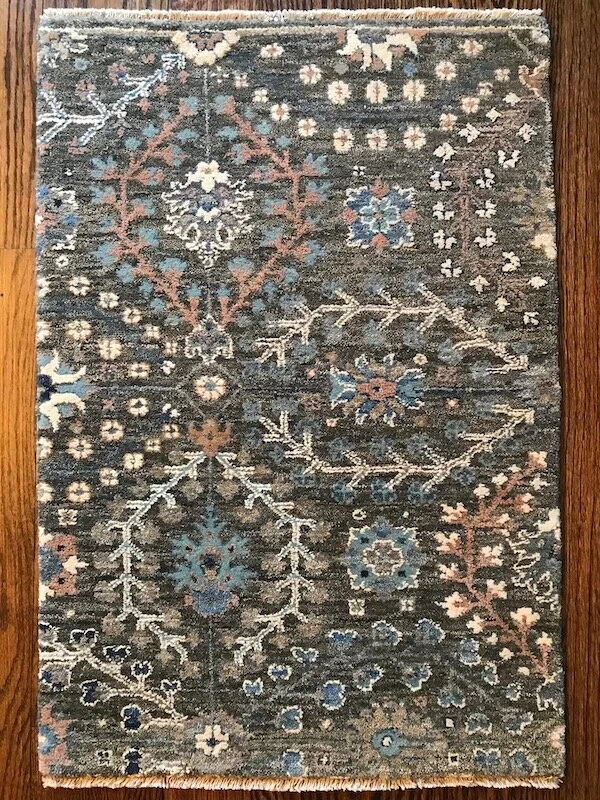 An area rug with a floral and geometric pattern in shades of blue, beige, and black, placed on a wooden floor.