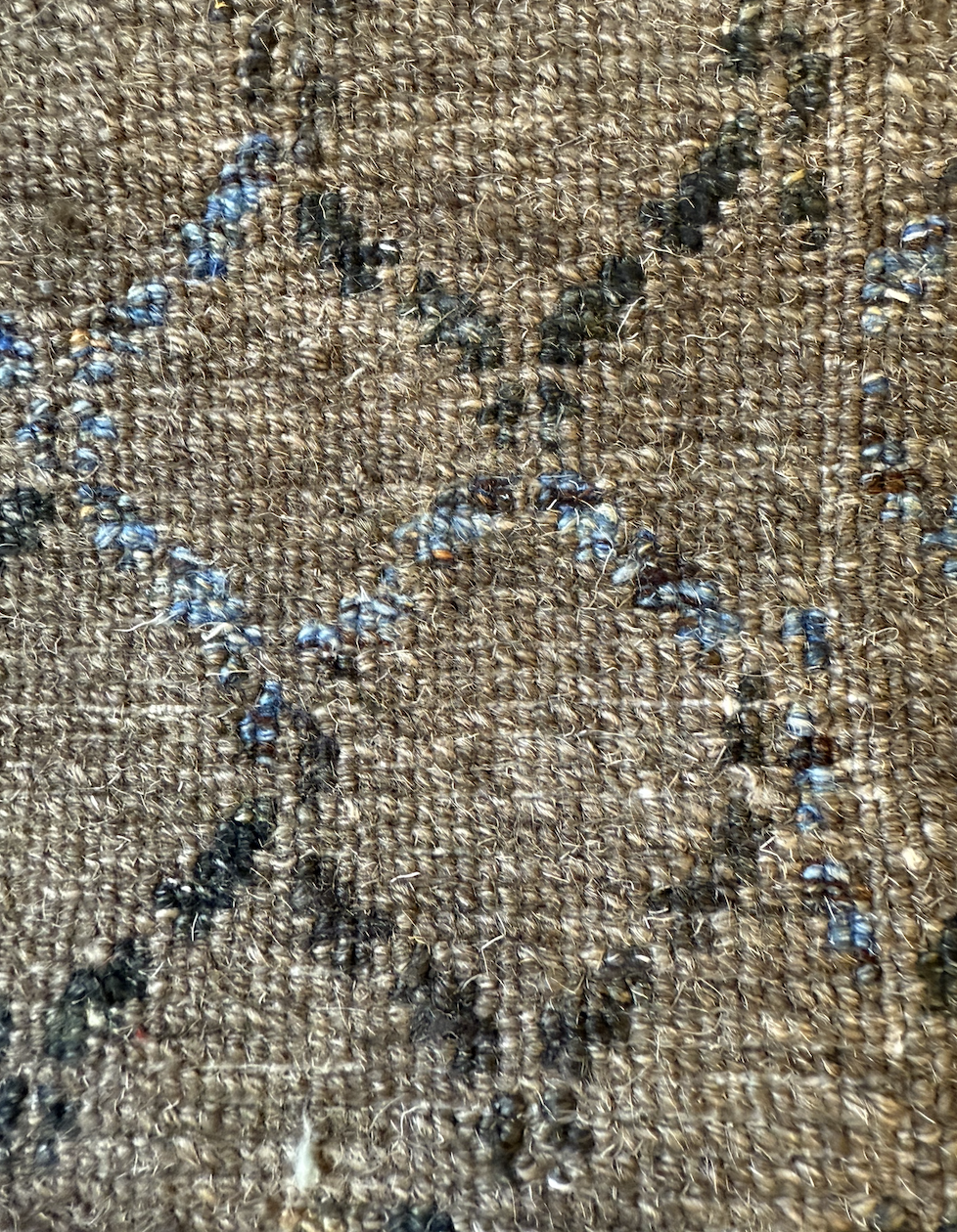 Close-up of a brown woven fabric with black and blue ink stains and splatters.