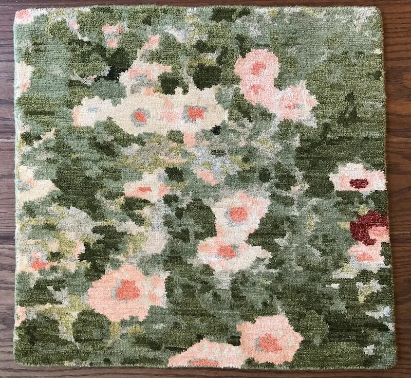 A floral patterned area rug with pink, red, white, and green colors placed on a wooden floor.