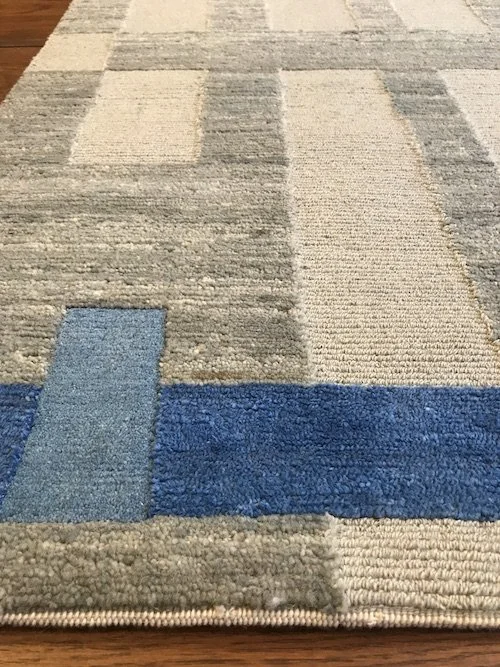 Close-up of a patterned area rug with beige, gray, and blue sections on a wooden floor.