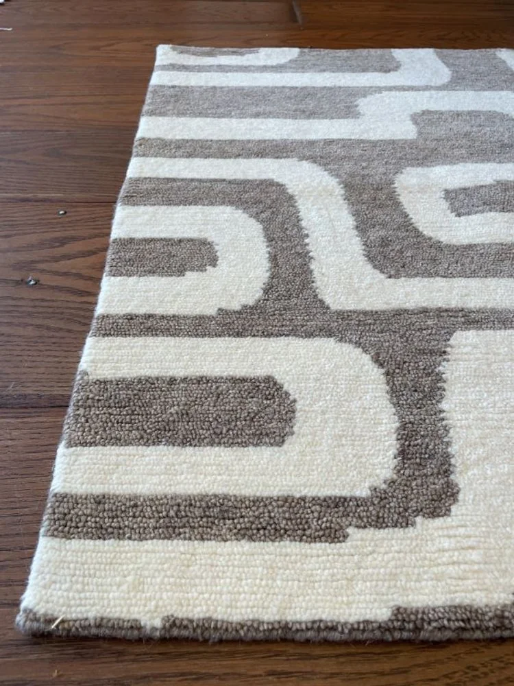 Close-up of a beige and brown patterned area rug on a hardwood floor.