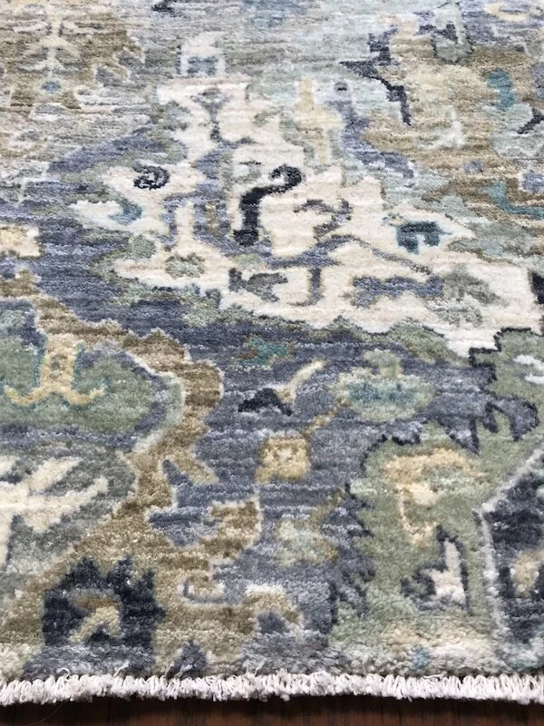 Close-up of a decorative area rug with an intricate pattern in shades of blue, green, beige, and cream.