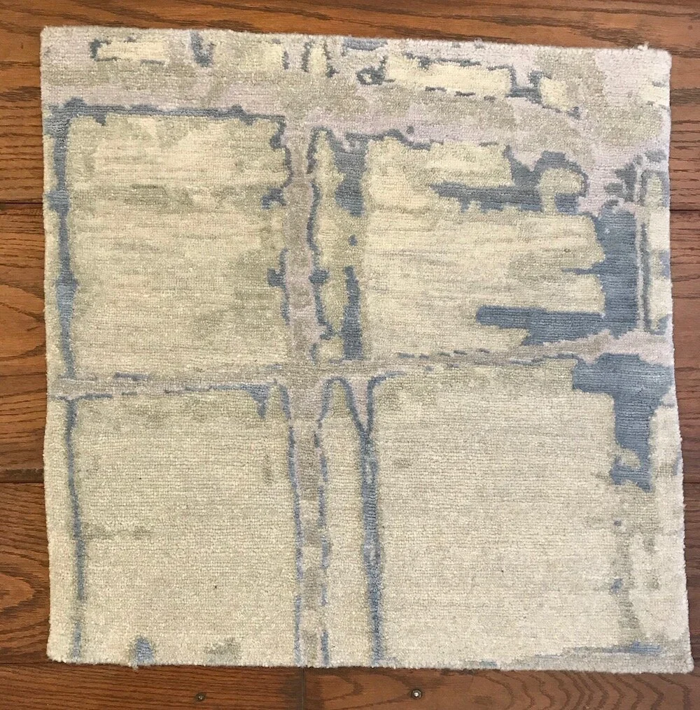 Light-colored area rug with an abstract, geometric pattern in muted shades of blue and beige, placed on a wooden floor.