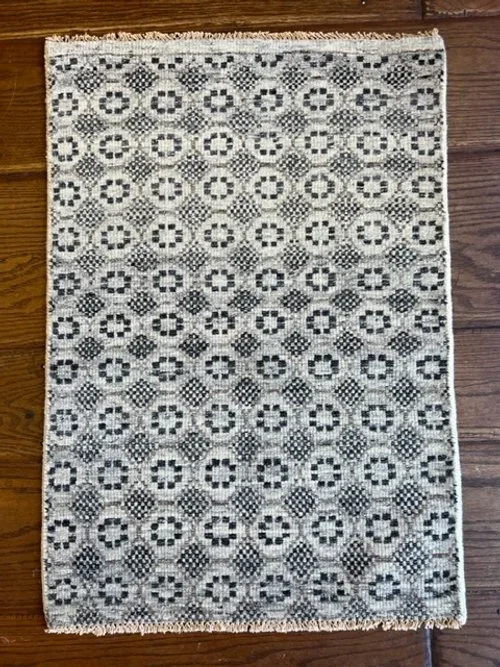 A small rectangular patterned rug with black and white geometric designs, placed on a wooden floor.