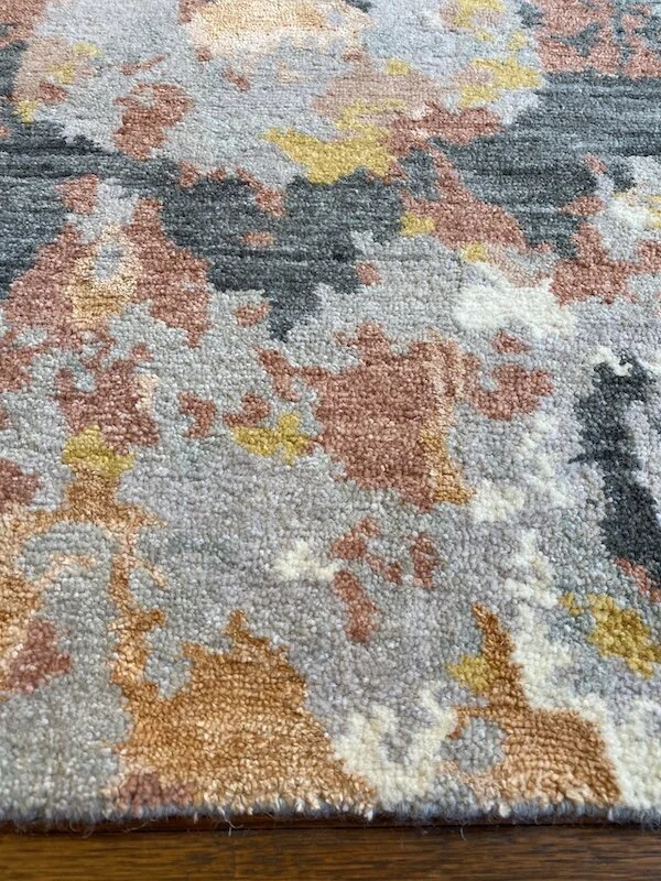Close-up of a multicolored abstract-patterned area rug with shades of blue, gray, yellow, peach, and cream.