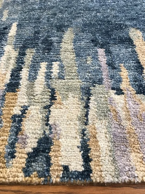 Close-up of a textured, multicolored abstract rug with shades of blue, beige, cream, pink, and purple.
