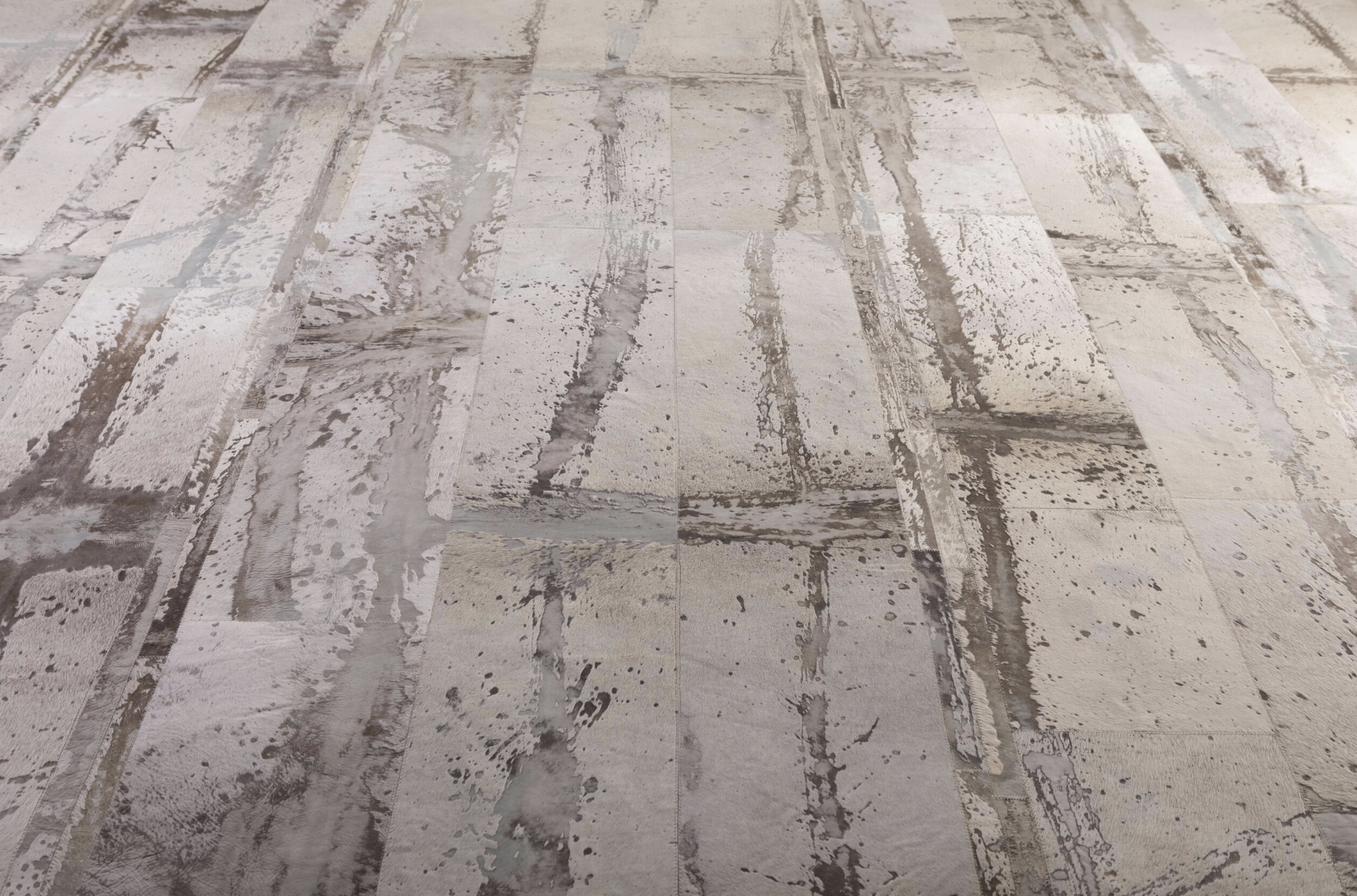 A close-up view of a patterned wooden or ceramic floor with a distressed, weathered appearance in shades of beige, brown, and gray.