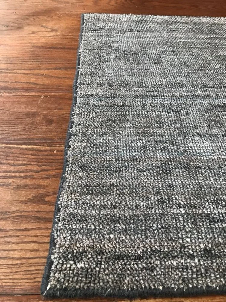 Close-up of a black, gray, and white textured rug on a wooden floor.