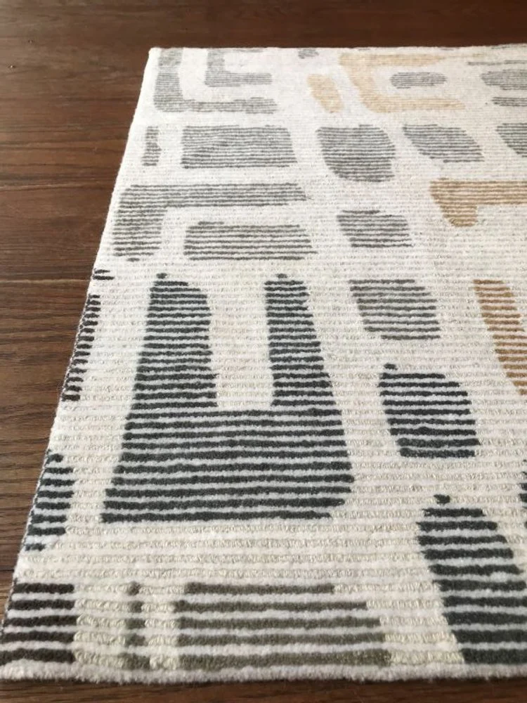 Close-up of a modern, geometric patterned area rug with black, white, gray, and beige rectangles and lines, placed on a hardwood floor.