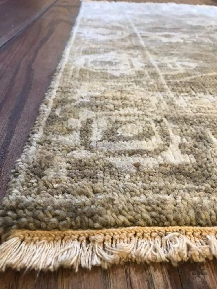 Close-up of a beige, textured area rug with fringed edges on a wooden floor.