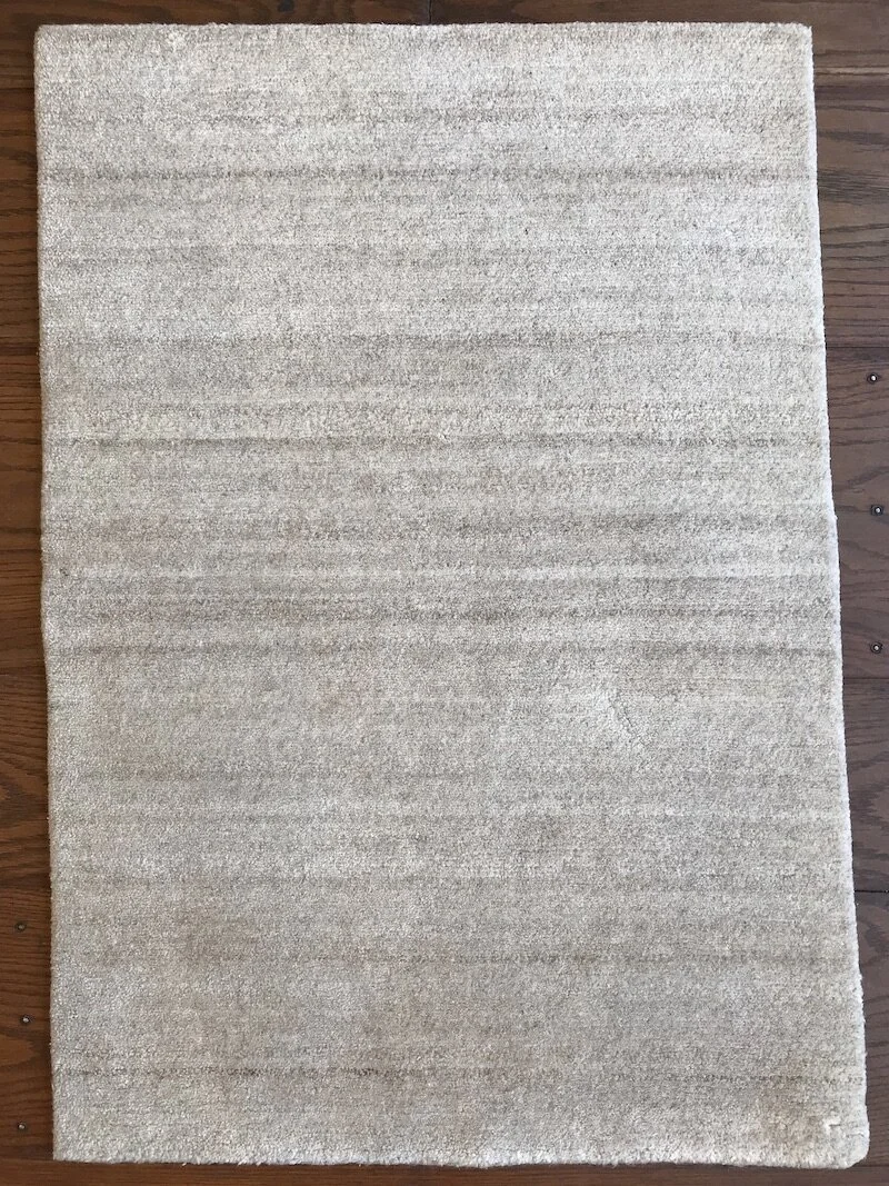 A beige plush area rug with horizontal stripe patterns placed on a wooden floor.