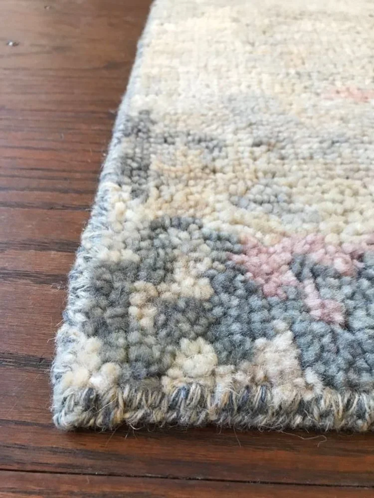 Close-up of the corner of a patterned area rug on a wooden floor, showing the woven edge and plush texture.