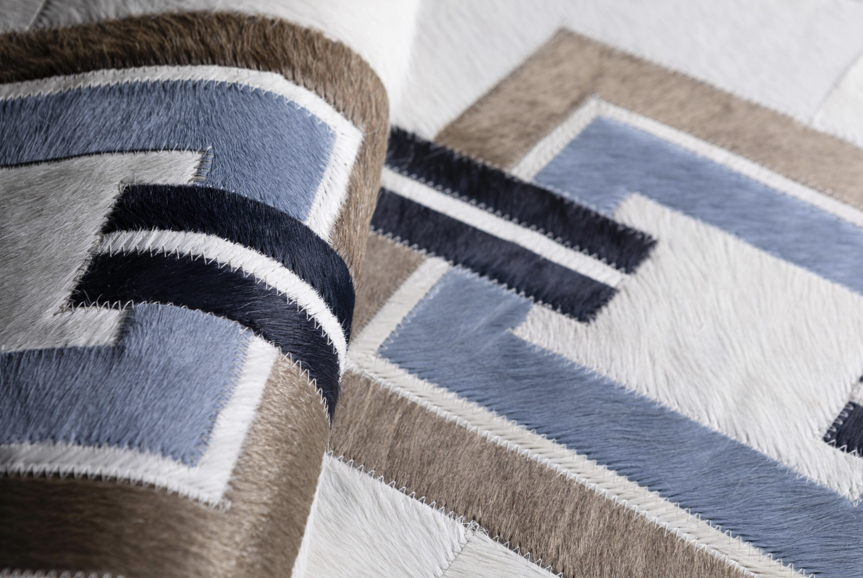 Close-up of a cowhide area rug with geometric patterns in shades of blue, black, white, and brown, laid on a white floor.