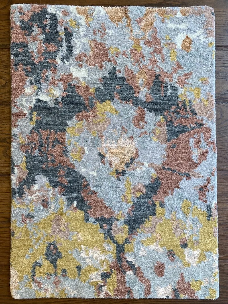 Colorful abstract patterned area rug with shades of blue, yellow, beige, and reddish-brown, placed on wooden floor.