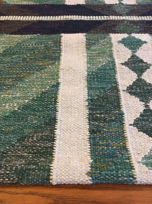 Close-up of a patterned woven rug featuring green, cream, and dark blue geometric designs.