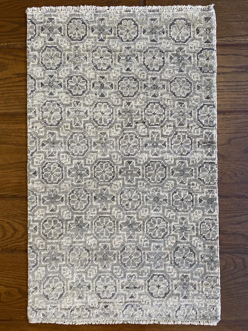 A rectangular area rug with a geometric pattern in shades of gray and beige, placed on a wooden floor.