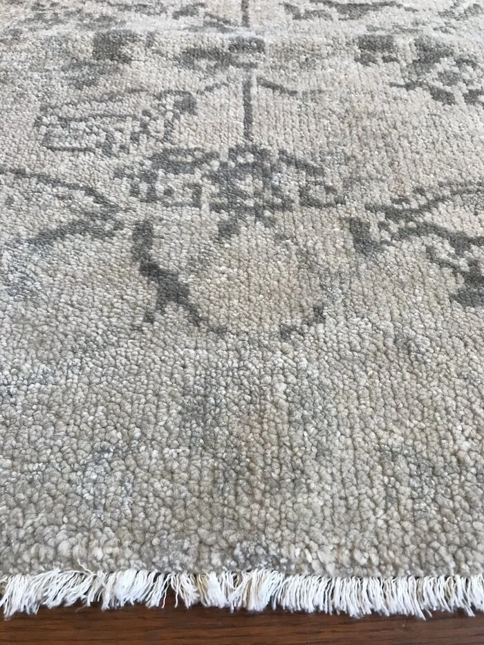 Close-up of a beige and gray patterned area rug on a wooden floor.